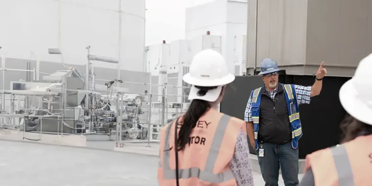 Facility tour group in hard hats at an industrial site.